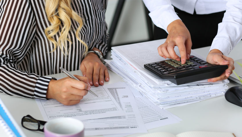 Two female accountants counting on calculator